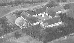 Nørrerisgaard fotograferet i 1936. Stuehuset i forgrunden ligger mod syd. Den vestre og den østre længe er oprindeligt opført af lerstampede vægge.